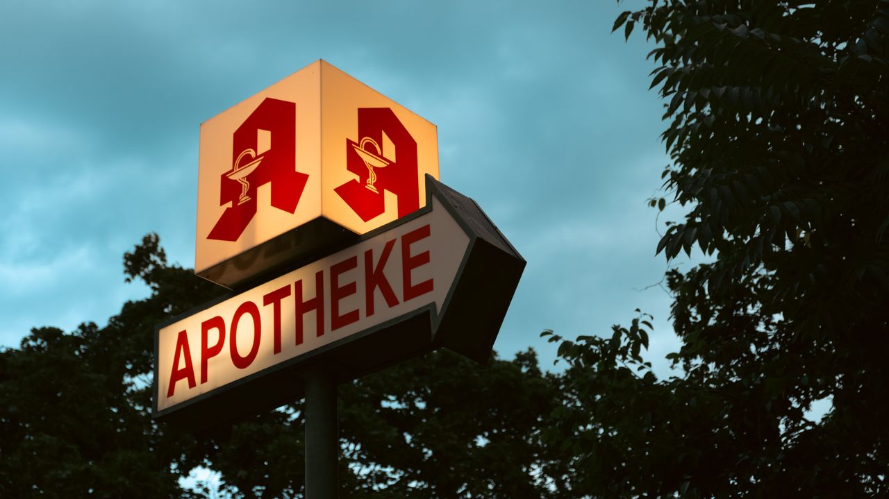 about-us Berlin pharmacy sign with iconic logo during twilight, surrounded by trees.